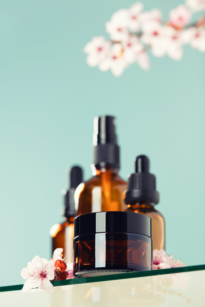 Amber glass bottles, cream jar and cherry blossom branches on green background. Skincare products , natural cosmetic. SPA natural organic beauty product packaging design, branding, low angle view, below the eye line, looking up, hero view