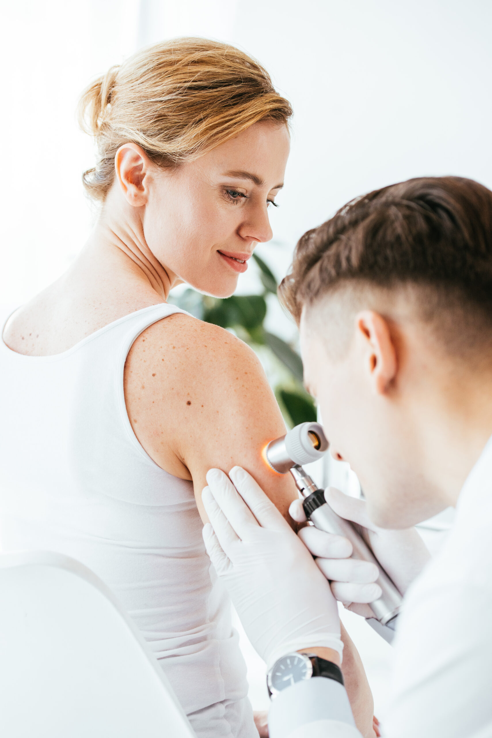 dermatologist in latex gloves holding dermatoscope while examining beautiful patient with skin