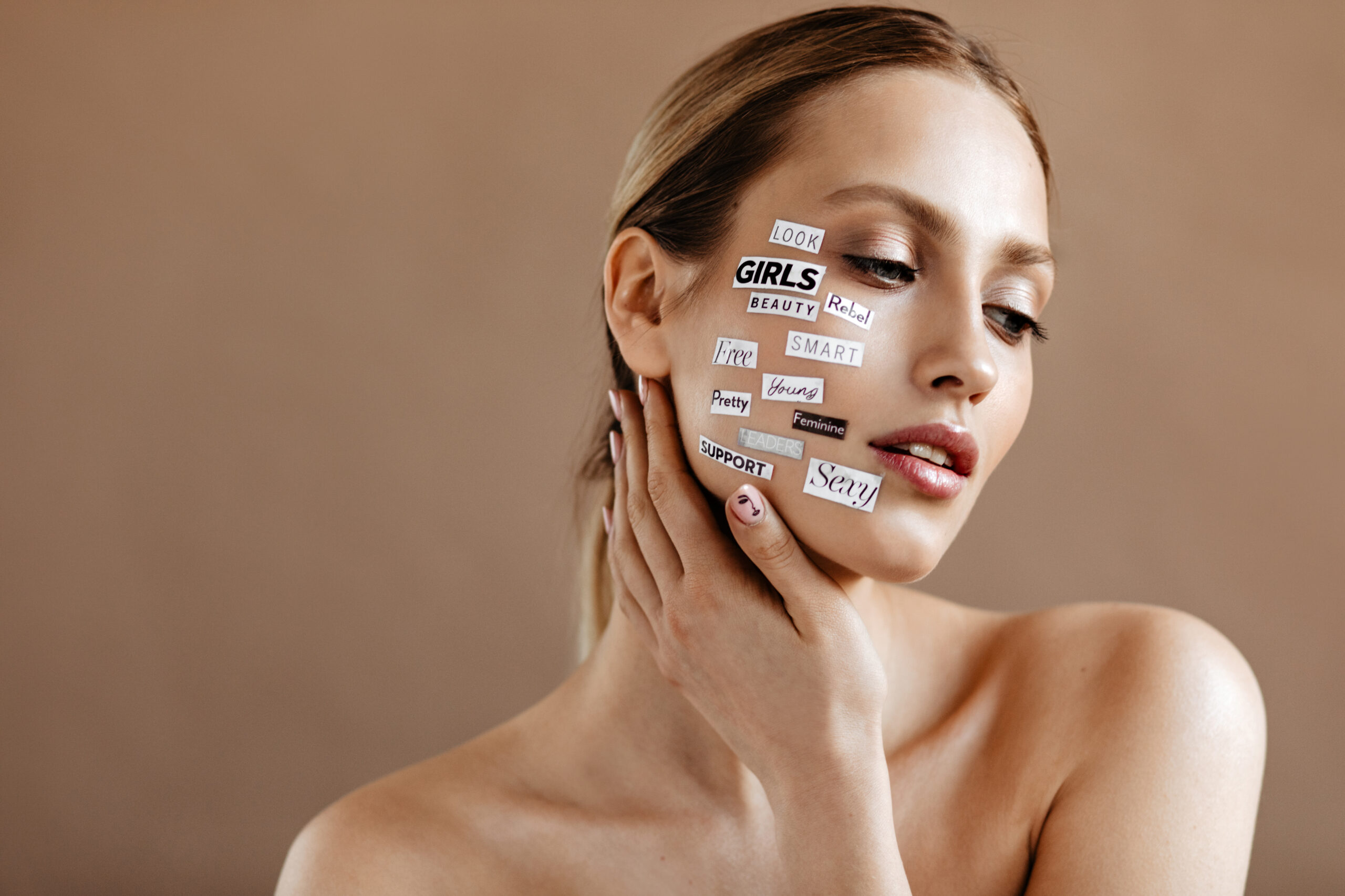 Girl with clear skin with white stickers-words on her face posing on beige background