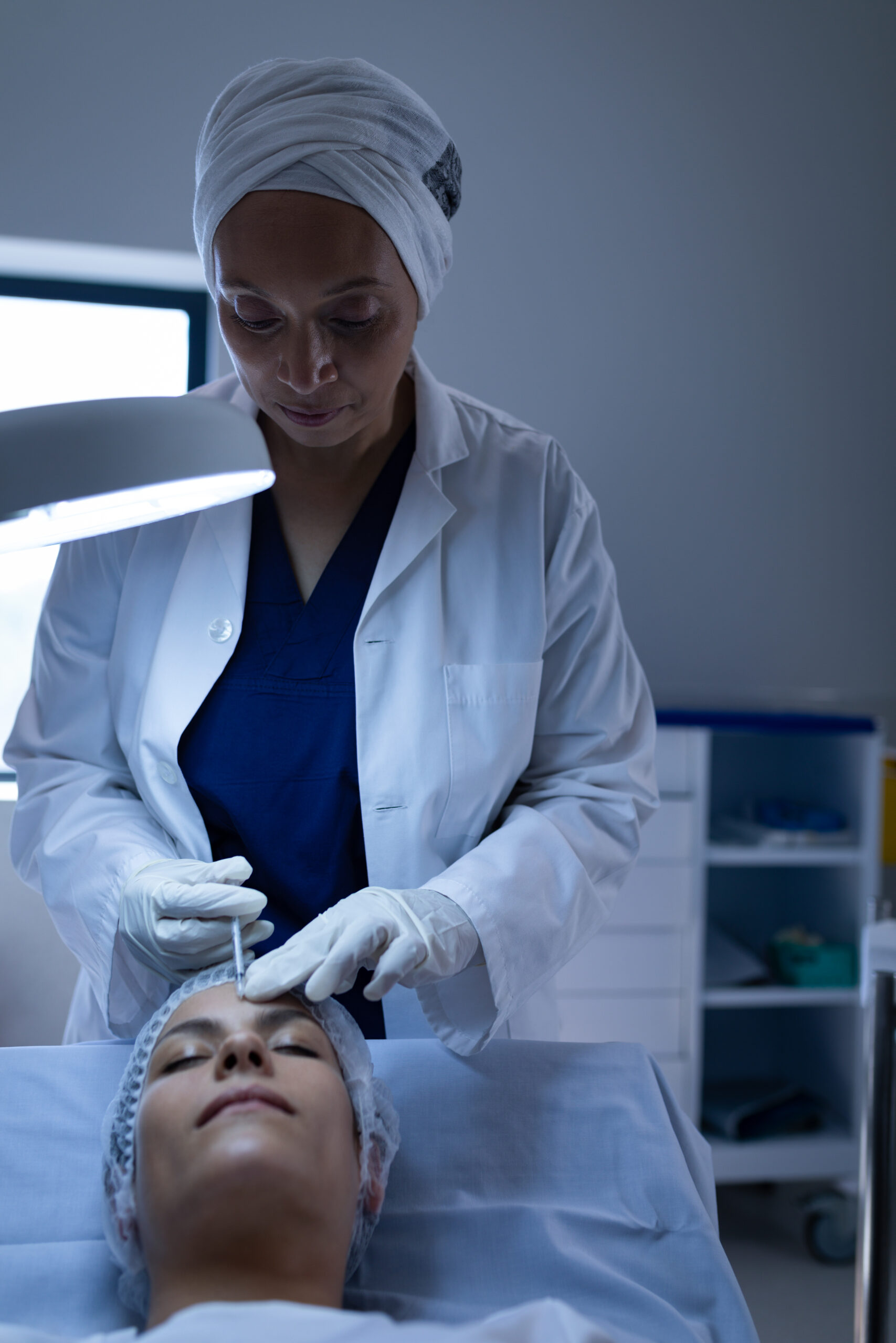 Front view of a female mixed-race surgeon giving plastic surgery injection on a Caucasian patient face