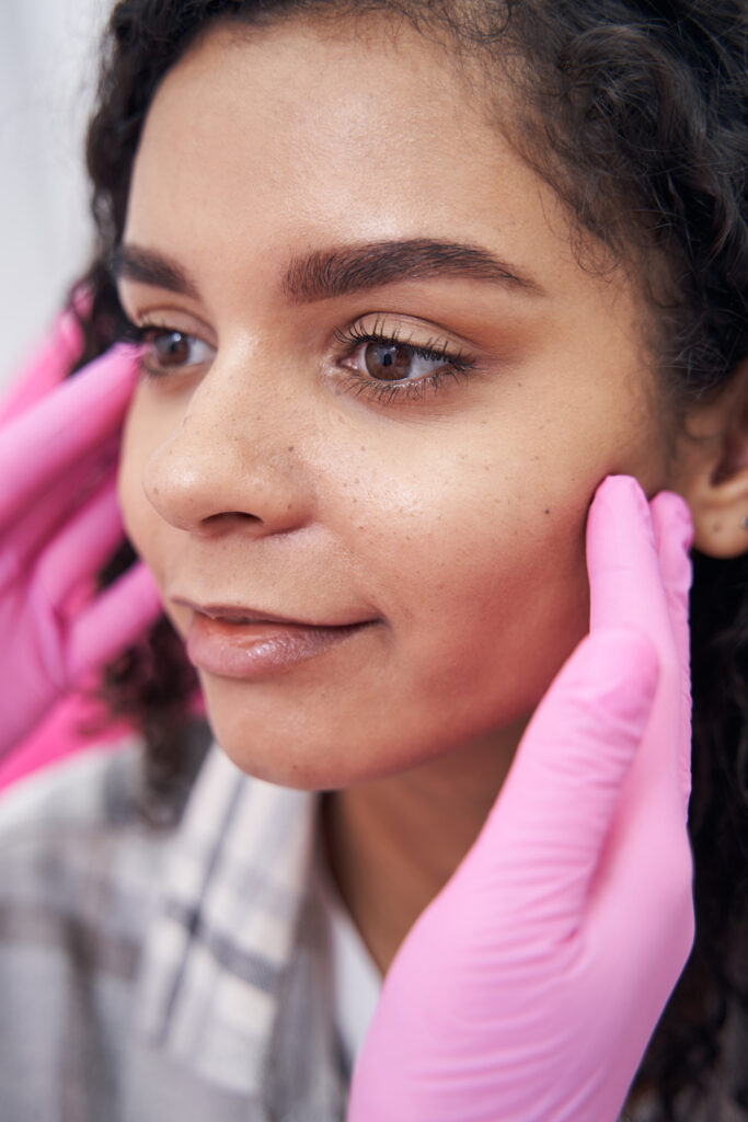 Encouraged lady with open eyes smiles while health worker touches her cheekbones with fingers
